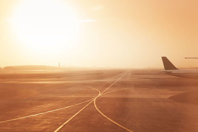 Airplane on airport runway against sky during sunset