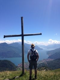 Rear view of man standing on grass by religious cross against sky