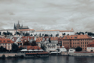 View of buildings by river against cloudy sky