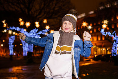 Portrait of young woman standing against illuminated christmas tree