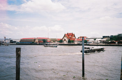 Wooden post in river by buildings against sky