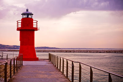 Lighthouse by sea against sky during sunset