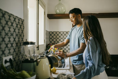 Young man and woman washing dishes together in kitchen sink at home