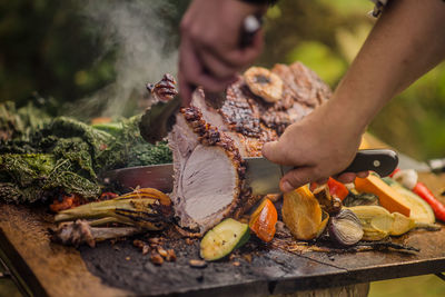 Master chef cuts roasted pork on bead of colourful vegetables in sunny green garden
