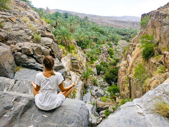 Rear view of woman sitting on rock by mountains