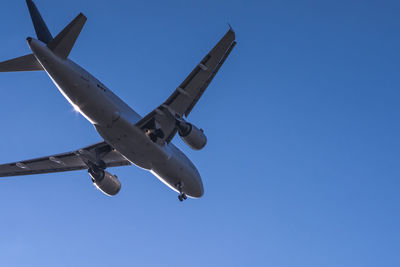 Low angle view of airplane against clear blue sky