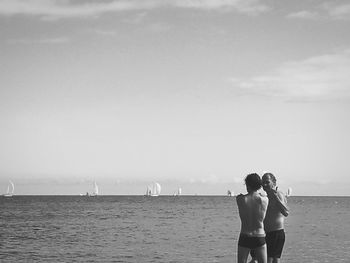 Rear view of women standing at beach against sky