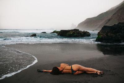 Rear view of woman lying on shore at beach against sky