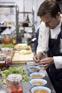 Chef garnishing soup with basil leaves at kitchen counter in restaurant