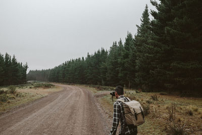 Rear view of man photographing on dirt road in forest