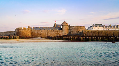 Old buildings by ocean surrounded by wall  against sky 