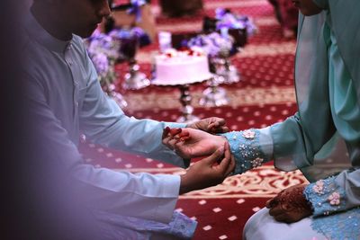 Midsection of groom tying bracelet on bride wrist during wedding ceremony