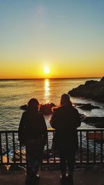 Rear view of silhouette man and woman standing at beach during sunset