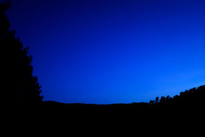 Silhouette landscape against clear blue sky at night