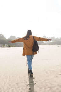 Carefree woman with arms outstretched walking on sand