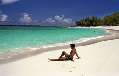 Full length of woman relaxing on beach against sky