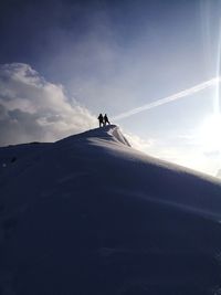 Low angle view of silhouette men standing on snowcapped mountain against sky
