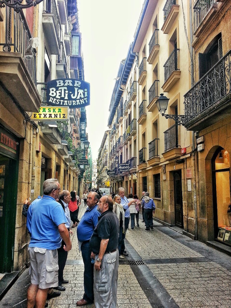 building exterior, architecture, built structure, street, men, city, person, lifestyles, walking, large group of people, city life, leisure activity, residential building, day, building, rear view, city street, residential structure, cobblestone