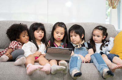 Friends using digital tablet while sitting on sofa