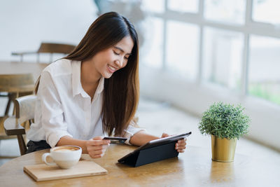 Young woman using phone while sitting on table