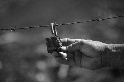 Close-up of hand holding padlock on barbed wire