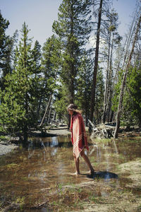 Woman wrapped in blanket walking on wet field against trees at yellowstone national park