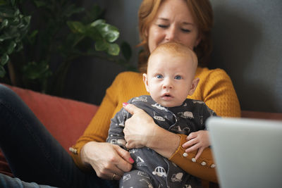 Happy grandmother holding baby grandson on sofa at home living room