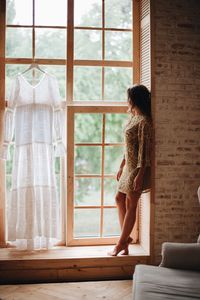 Full length of woman looking through window at home