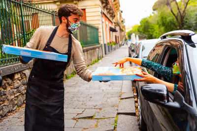 Closeup hipster delivery man wearing medical protective, holding paper shopping bags in hands. 