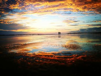 Silhouette people standing on beach against sky during sunset