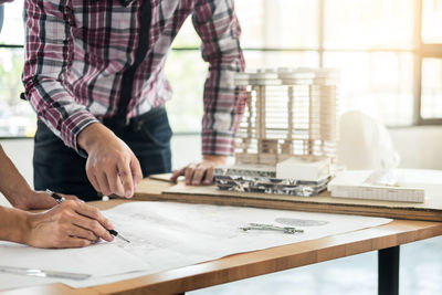 Midsection of architects discussing over blueprint on table
