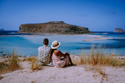 Rear view of woman sitting on beach against sky