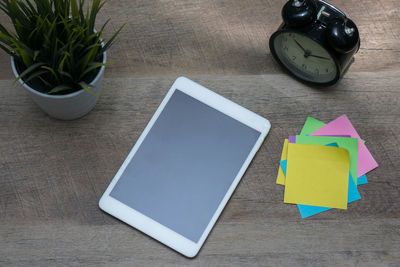 High angle view of digital tablet with colorful adhesive notes by plant and alarm clock on wooden table