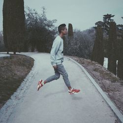 Side view of man jumping on walkway in park