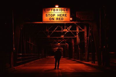 Rear view of silhouette man standing on illuminated bridge at night