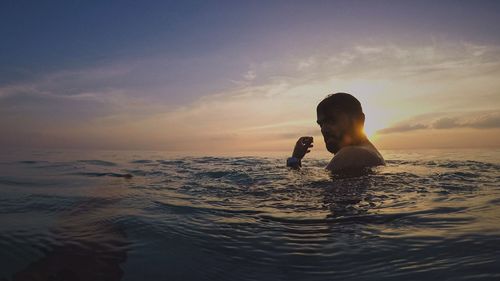 Portrait of man swimming in sea against sky during sunset