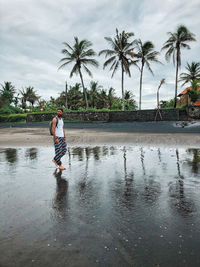 Full length of man walking on beach against palm trees