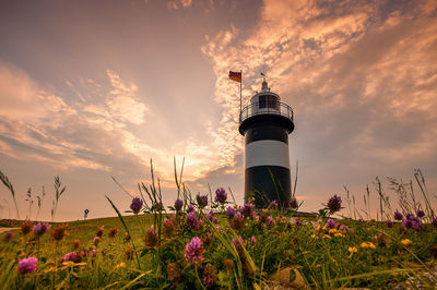 Lighthouse amidst plants and building against sky during sunset