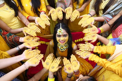 Portrait of smiling bride surrounded with females showing henna tattoo at haldi ceremony