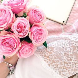 Cropped hand of bride holding rose bouquet on bed