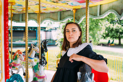 Beautiful brunette girl in a black dress poses on a bright carousel with horses