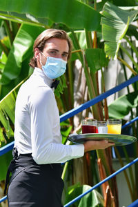 Portrait of waiter holding juice against plants