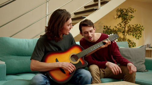 Homosexual couple playing guitar at home