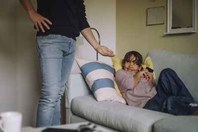 Midsection of father asking smart phone from daughter sitting on sofa at home