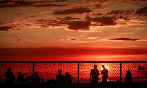 Silhouette people by sea against sky during sunset