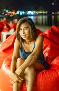 Portrait of smiling woman sitting on bean bag in city at night