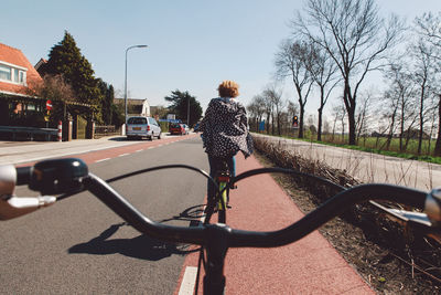 Cropped image of bicycle against woman on road during sunny day