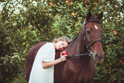 Portrait of woman holding apple standing by horse