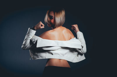 Rear view of seductive woman wearing jacket standing against black background
