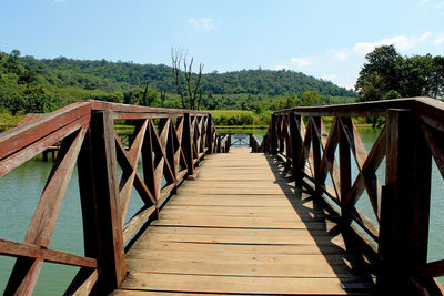 Wooden footbridge in forest against sky